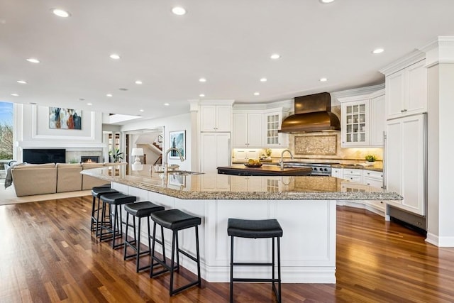 kitchen featuring a large island, a breakfast bar area, a lit fireplace, premium range hood, and a sink