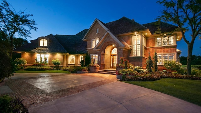 view of front of house featuring decorative driveway, french doors, brick siding, and a front lawn