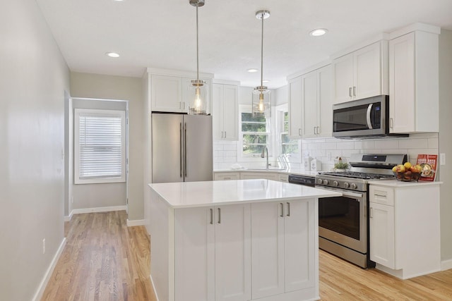 kitchen with a kitchen island, white cabinets, light countertops, appliances with stainless steel finishes, and decorative light fixtures