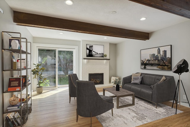 living area featuring a textured ceiling, recessed lighting, a brick fireplace, light wood finished floors, and beamed ceiling