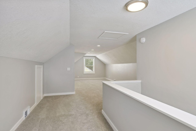 additional living space featuring a textured ceiling, lofted ceiling, light carpet, visible vents, and baseboards