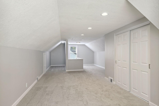 additional living space with a textured ceiling, lofted ceiling, light colored carpet, visible vents, and baseboards