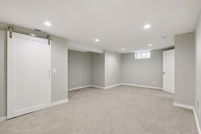 below grade area with light carpet, a barn door, visible vents, and recessed lighting