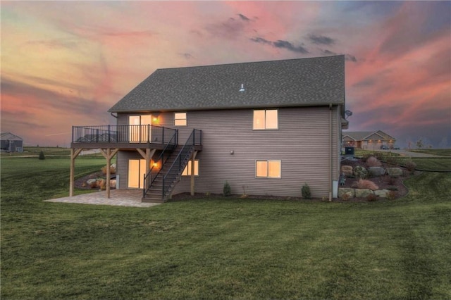 back house at dusk with a wooden deck, a patio area, and a lawn