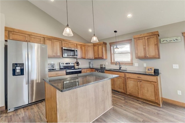 kitchen with appliances with stainless steel finishes, decorative light fixtures, sink, a center island, and light hardwood / wood-style flooring