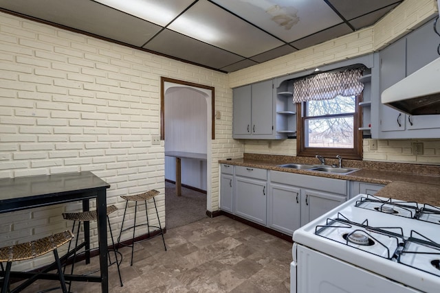 kitchen featuring brick wall, white range with gas cooktop, sink, and a drop ceiling