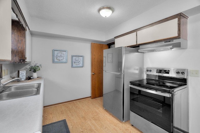 kitchen with stainless steel appliances, white cabinets, a sink, light wood-type flooring, and under cabinet range hood