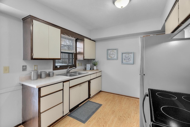 kitchen featuring light countertops, electric range, freestanding refrigerator, a sink, and light wood-type flooring