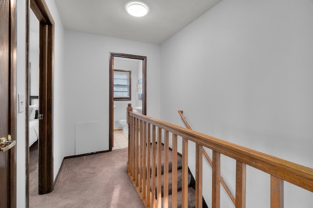 hallway with light carpet, a textured ceiling, and an upstairs landing