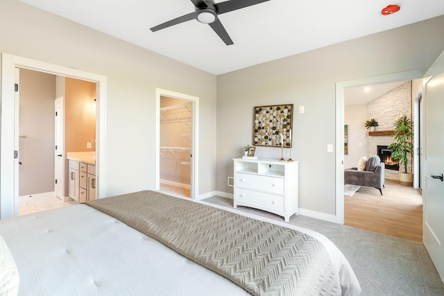 carpeted bedroom featuring ceiling fan, a walk in closet, a fireplace, and ensuite bath