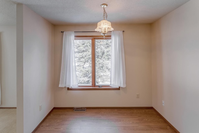 spare room with a textured ceiling, light hardwood / wood-style floors, an inviting chandelier, and plenty of natural light