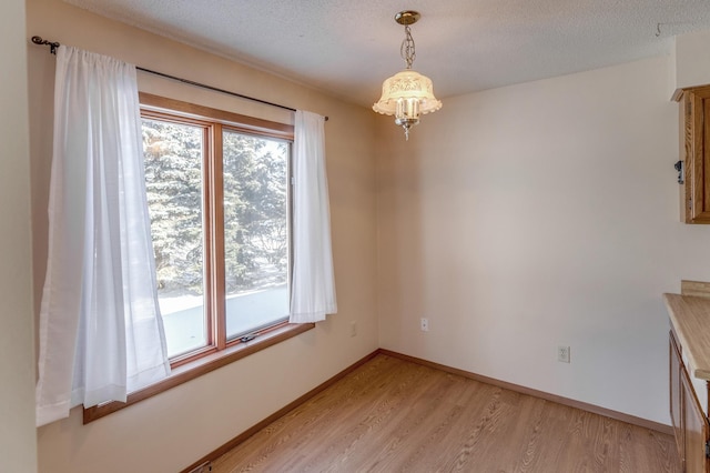 unfurnished dining area featuring light hardwood / wood-style floors, an inviting chandelier, and a textured ceiling