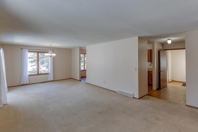 spare room featuring light carpet, a textured ceiling, and a notable chandelier