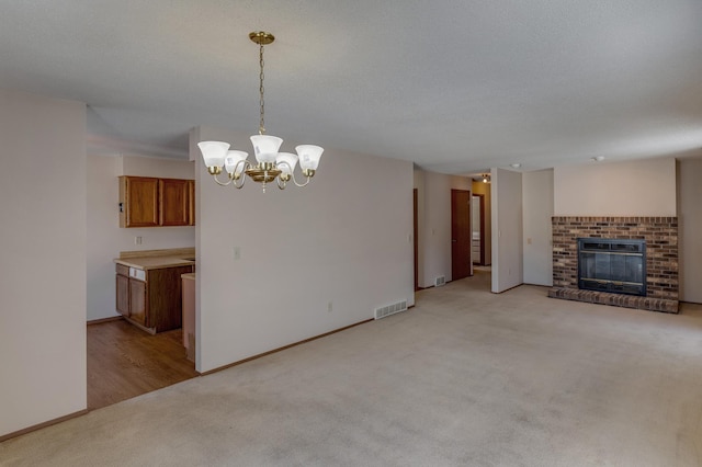 unfurnished living room featuring light carpet, a chandelier, a textured ceiling, and a brick fireplace