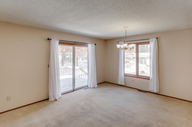 empty room featuring a notable chandelier, a textured ceiling, and light colored carpet