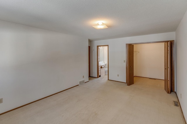 unfurnished bedroom with light carpet, ensuite bath, a spacious closet, and a textured ceiling