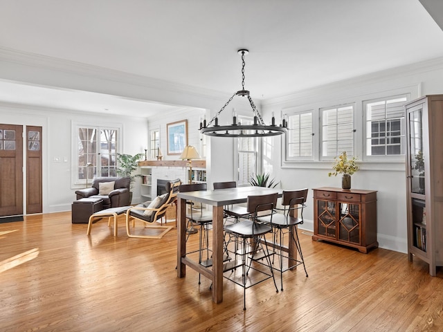 dining space featuring a brick fireplace, light hardwood / wood-style flooring, and ornamental molding