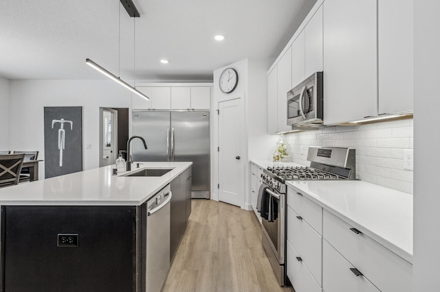 kitchen with pendant lighting, sink, appliances with stainless steel finishes, a kitchen island with sink, and white cabinets