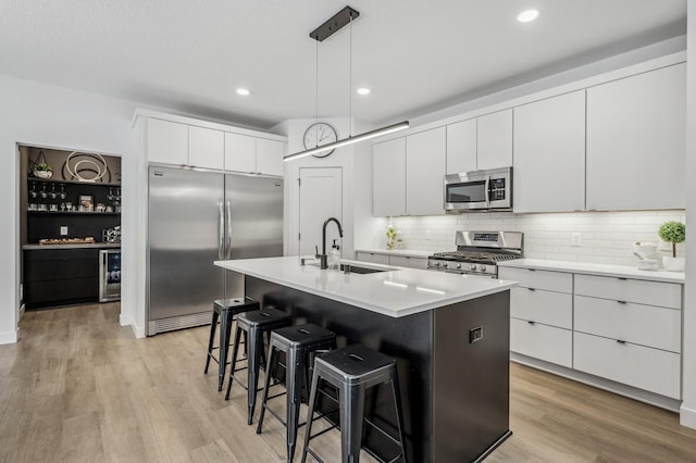 kitchen featuring sink, white cabinetry, a center island with sink, appliances with stainless steel finishes, and pendant lighting