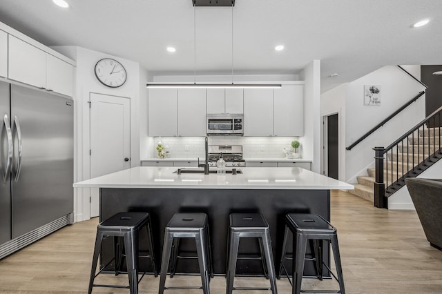 kitchen with appliances with stainless steel finishes, a kitchen island with sink, sink, and white cabinets