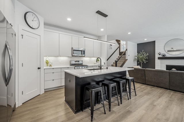 kitchen with hanging light fixtures, a center island with sink, a kitchen breakfast bar, stainless steel appliances, and white cabinets