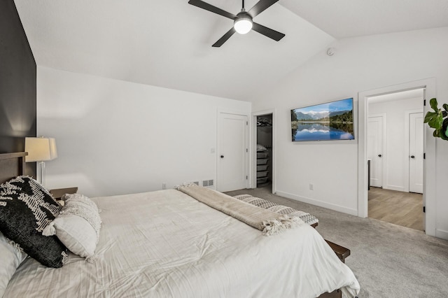 carpeted bedroom with vaulted ceiling, a walk in closet, and ceiling fan