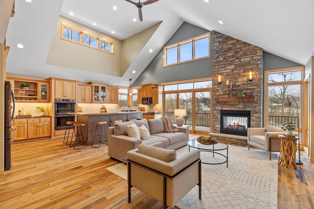 living room featuring lofted ceiling, sink, a stone fireplace, and light wood-type flooring