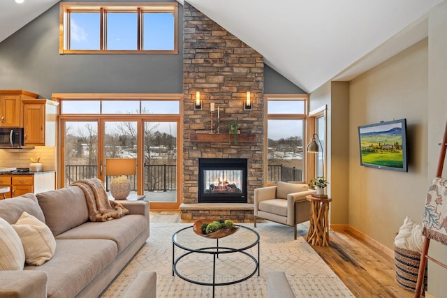 living room featuring high vaulted ceiling, a stone fireplace, and light hardwood / wood-style floors