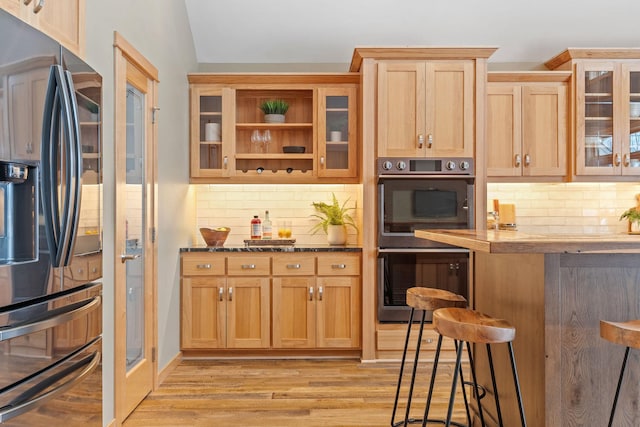 kitchen with a breakfast bar, light hardwood / wood-style flooring, double wall oven, stainless steel fridge, and backsplash