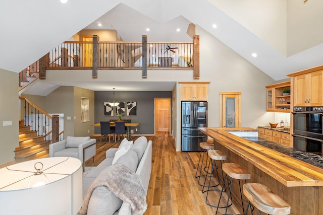 kitchen featuring stainless steel refrigerator with ice dispenser, wood counters, high vaulted ceiling, light wood-type flooring, and black double oven