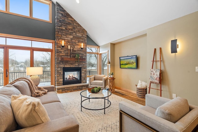 living room featuring wood-type flooring, a stone fireplace, high vaulted ceiling, and plenty of natural light