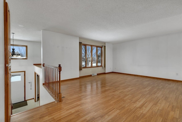 spare room with a chandelier, a textured ceiling, and light wood-type flooring