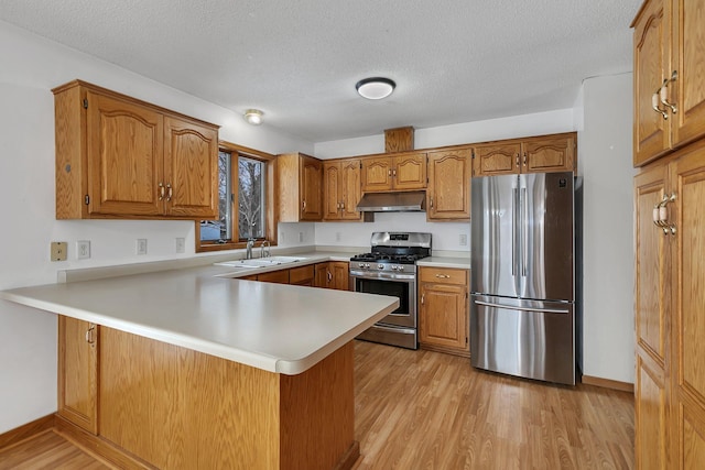 kitchen with sink, a textured ceiling, light wood-type flooring, appliances with stainless steel finishes, and kitchen peninsula