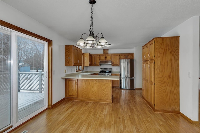 kitchen featuring appliances with stainless steel finishes, sink, hanging light fixtures, kitchen peninsula, and light hardwood / wood-style flooring