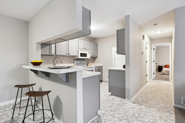 kitchen featuring sink, a breakfast bar area, gray cabinets, kitchen peninsula, and white appliances