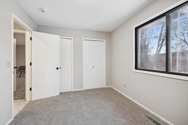 unfurnished bedroom featuring two closets and light colored carpet