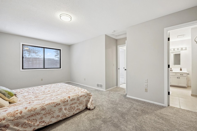 carpeted bedroom featuring a textured ceiling and ensuite bath