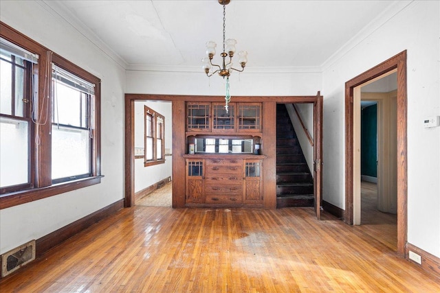 unfurnished dining area featuring a notable chandelier, crown molding, and wood-type flooring