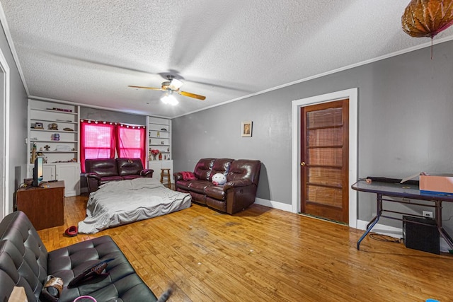 living room featuring built in shelves, a textured ceiling, ornamental molding, ceiling fan, and hardwood / wood-style floors