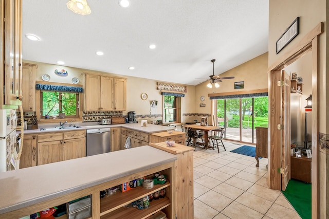 kitchen with light tile patterned flooring, vaulted ceiling, light brown cabinetry, sink, and stainless steel dishwasher