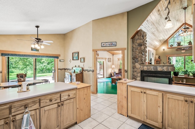 kitchen featuring vaulted ceiling, a stone fireplace, light tile patterned flooring, ceiling fan, and light brown cabinets