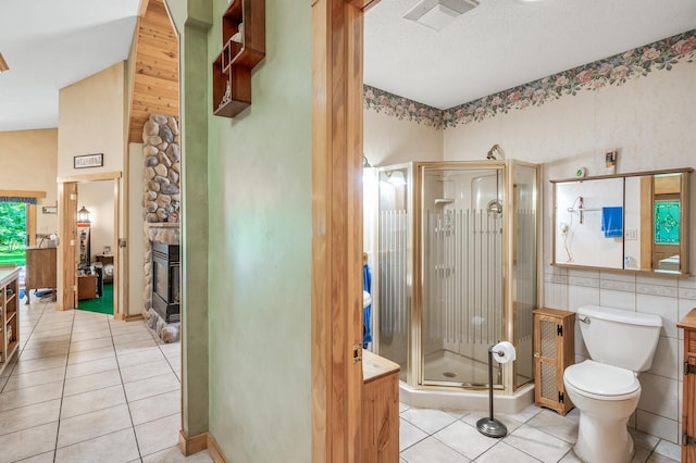 bathroom with tile patterned floors, toilet, a stone fireplace, tile walls, and a shower with door