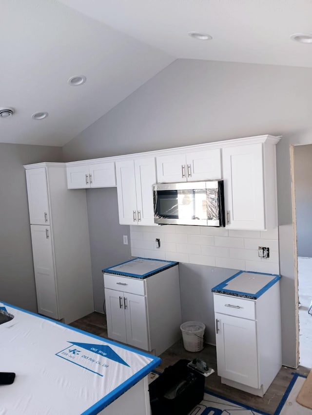 kitchen with vaulted ceiling, dark wood-type flooring, white cabinets, and decorative backsplash