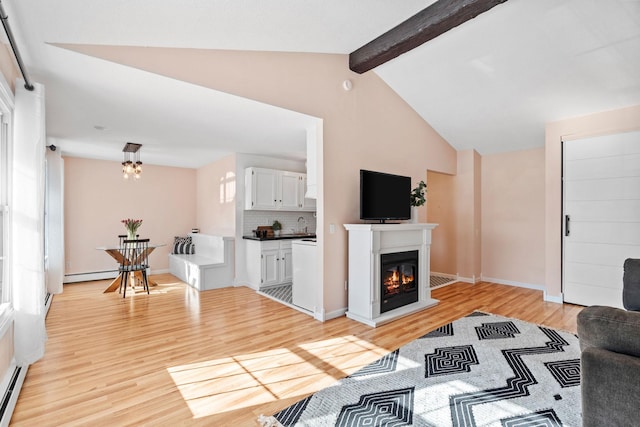 living room with vaulted ceiling with beams, light wood finished floors, a wealth of natural light, and a glass covered fireplace