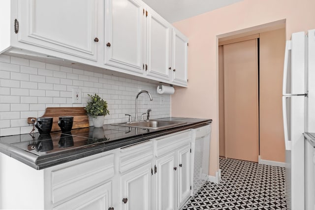 kitchen with tasteful backsplash, dark countertops, white cabinets, a sink, and white appliances