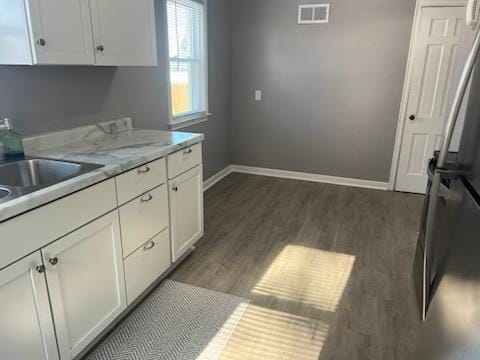 kitchen featuring stainless steel refrigerator, dark hardwood / wood-style floors, light stone countertops, and white cabinets