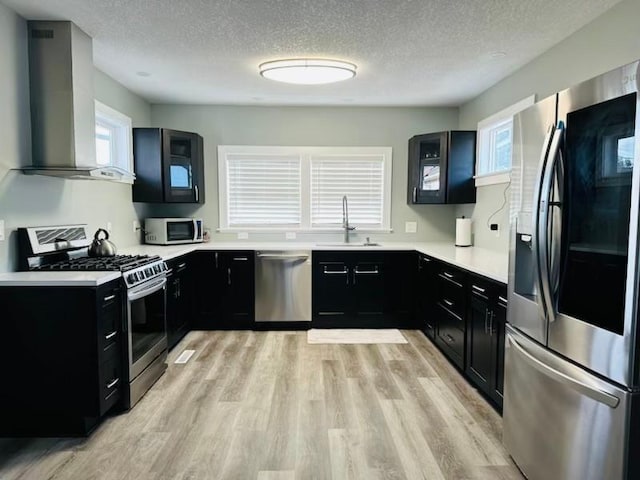 kitchen featuring sink, wall chimney exhaust hood, stainless steel appliances, a textured ceiling, and light hardwood / wood-style flooring