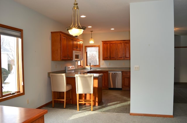 kitchen featuring a kitchen bar, sink, appliances with stainless steel finishes, kitchen peninsula, and pendant lighting