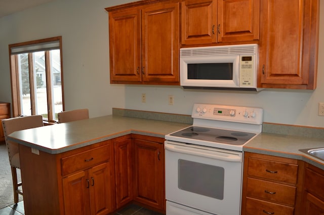 kitchen with white appliances, a kitchen breakfast bar, kitchen peninsula, and sink