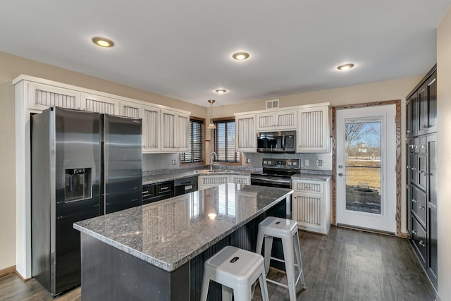 kitchen featuring decorative backsplash, dark wood finished floors, appliances with stainless steel finishes, dark stone countertops, and a sink